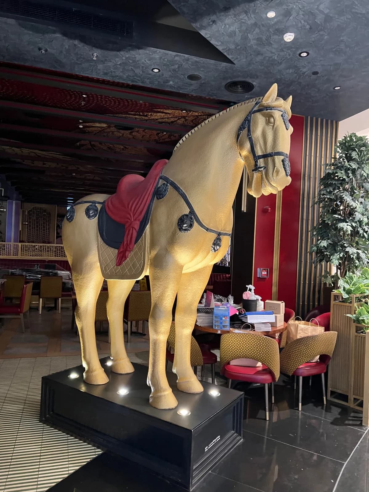 Gold-coloured decorative horse sculpture with red saddle on an illuminated black plinth.