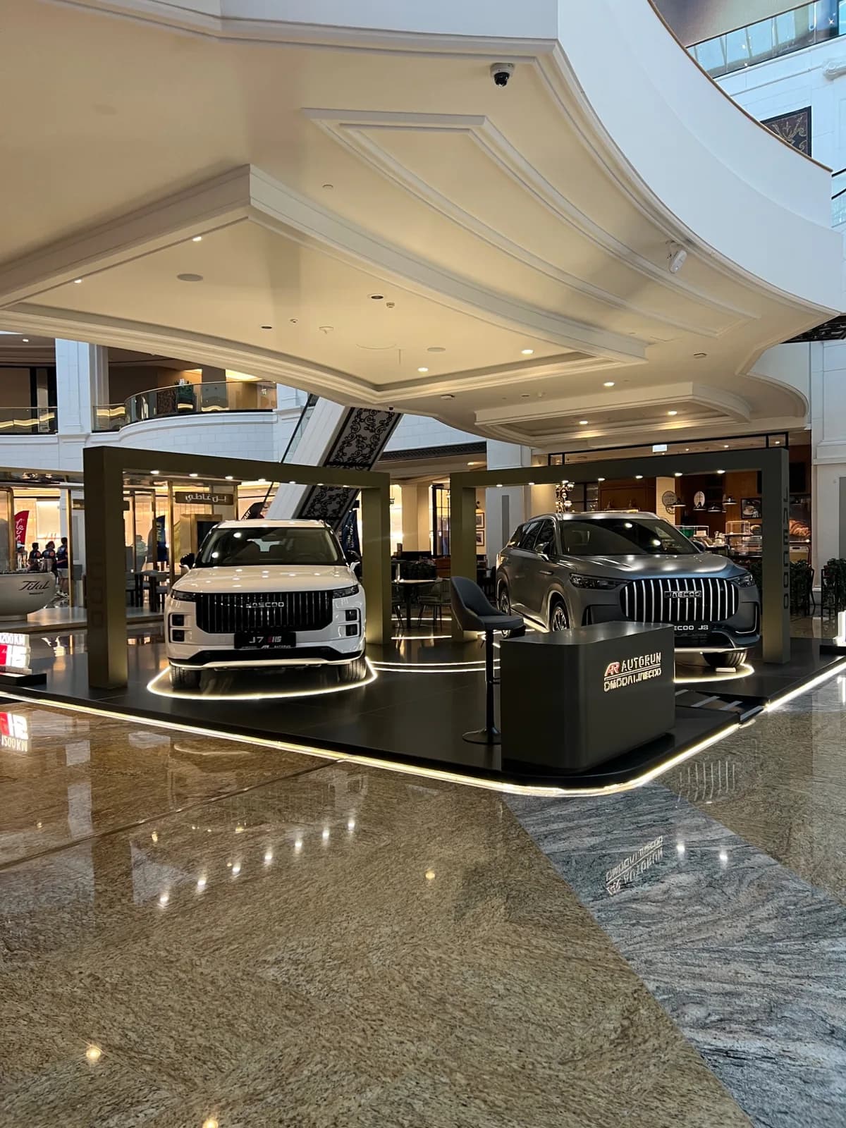 Two JAECOO vehicles on an illuminated black platform with an AUTOGRUN branded counter.