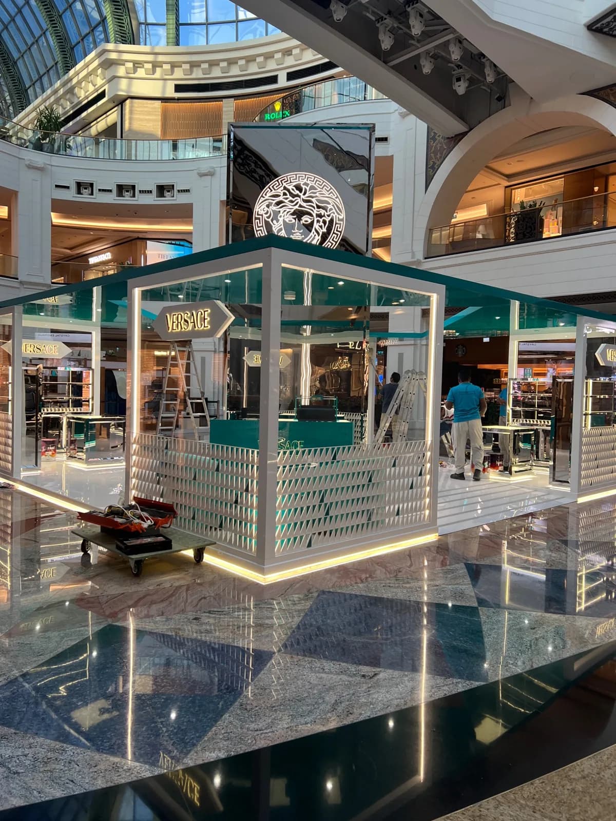 Versace kiosk with turquoise canopy, illuminated Medusa sign and ladders inside.